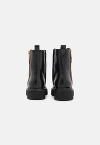 Stivaletti neri in pelle, con un pannello laterale marrone testurizzato, dettagli in cerniera dorata e una suola nera spessa. Finitura liscia con cuciture a contrasto.