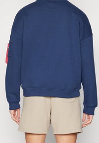 Felpa blu navy in cotone misto, con spalle scese e tasca sulla manica sinistra. Abbinala a pantaloni shorts beige.