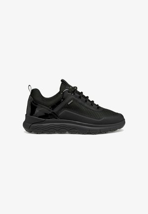 Zapatilla deportiva negra con parte superior de malla, acentos brillantes, cuello acolchado, cierre de cordones y suela texturizada con patrón de olas.
