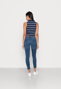 Top cropped sem mangas com riscas náuticas e jeans justo azuis, combinado com ténis brancos. Tecido suave com uma silhueta ajustada e detalhes mínimos.