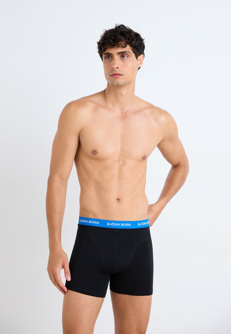 Schwarze Boxershorts mit einem blauen "BJÖRN BORG"-Bund. Der Stoff ist glatt und hat eine figurbetonte Form, mit flachen Nähten und einem Standard-Schnitt.