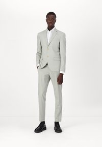 Šviesiai pilkas kostiumas su vieno sagos švarku, notch apykaklėmis, priekinėmis kišenėmis ir auksinėmis sagomis. Derinamas su balta marškiniais ir juodais batais.