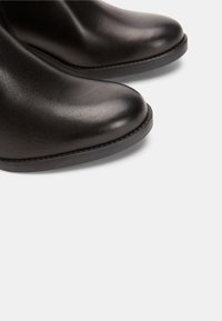 Stivali alla caviglia in pelle nera con punta arrotondata, superficie liscia e dettagli di cucitura minimi. Suola piatta in gomma. Nessun accento hardware visibile.