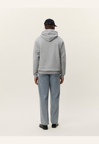 Grijze hoodie met een trekkoord, weergegeven vanaf de achterkant. Combinatie met lichtblauwe, losse spijkerbroek en zwarte schoenen.