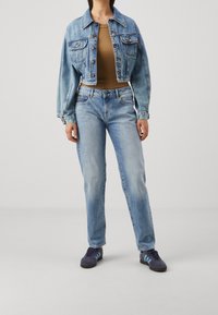 Ljusblå jeansjacka med två bröstfickor, kombinerad med en beige topp och ljusblå raka jeans. Svarta och blå sneakers fulländar looken.