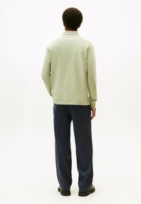 Camisa polo de manga larga, color verde claro, con cuello, combinada con pantalones de piernas anchas color azul oscuro. Textura de tela suave y corte relajado.