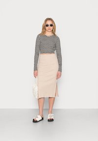 Schwarzes und weißes gepunktetes Cropped-Top, beiger gerippter Midirock, weiße Sandalen mit schwarzen Sohlen und eine strukturierte weiße Handtasche.