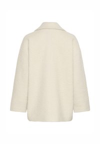 Manteau beige texturé à coupe décontractée, col à revers et manches trois-quarts, présentant une surface à motif subtil.