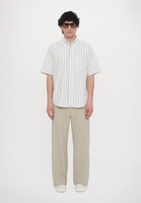 Kortermet hvit skjorte med vertikale grå striper, kombinert med lysebeige, løstsittende bukser og hvite joggesko.