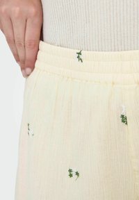 Falda amarillo claro con cintura elástica fruncida, que presenta delicados bordados florales en verde y blanco sobre una tela texturizada.