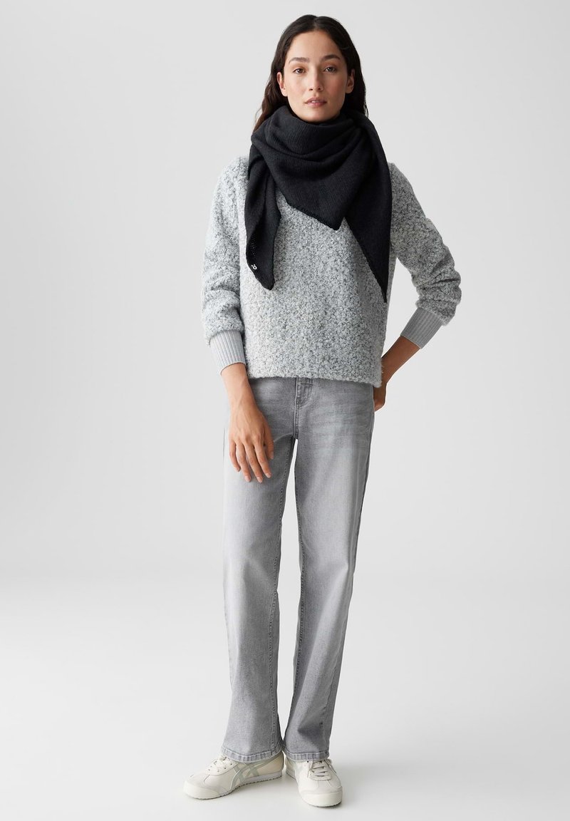 Lichtgrijze textuurtrui, donkergrijze sjaal, lichtgrijze jeans en witte sneakers. Casual, gelaagd outfit met een ontspannen pasvorm.
