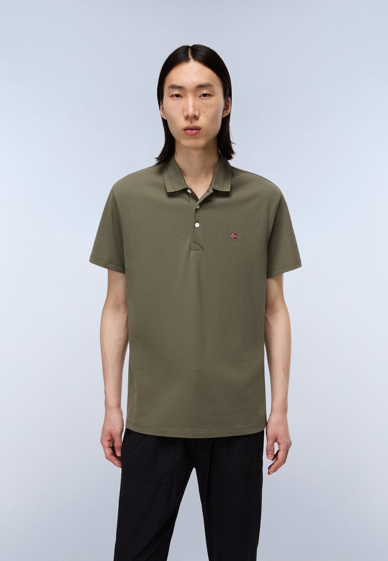 Polo shirt a maniche corte di colore oliva con colletto a tre bottoni, piccolo patch ricamato sul petto e vestibilità comoda. Tessuto morbido.