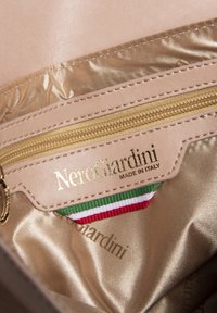 Intérieur en cuir rose clair avec fermeture éclair dorée et éclat métallique. Présente le logo "Nero Giardini" et des couleurs du drapeau italien en accent.