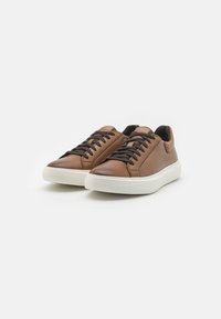 Zapatillas de cuero marrón con una textura suave, que presentan cordones negros, una suela de goma blanca y un diseño minimalista.