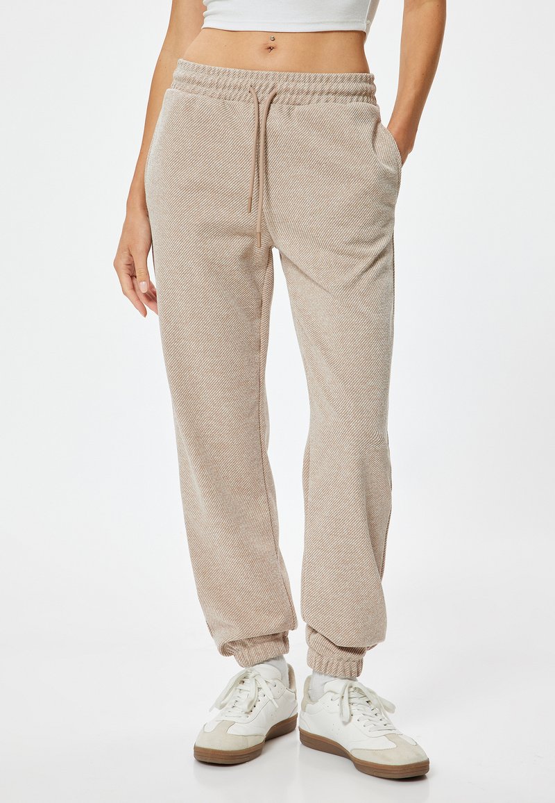Helle beige Sweatpants mit einem strukturierten Muster, elastischem Bund mit Kordelzug, seitlichen Taschen und elastischen Bündchen an den Knöcheln.