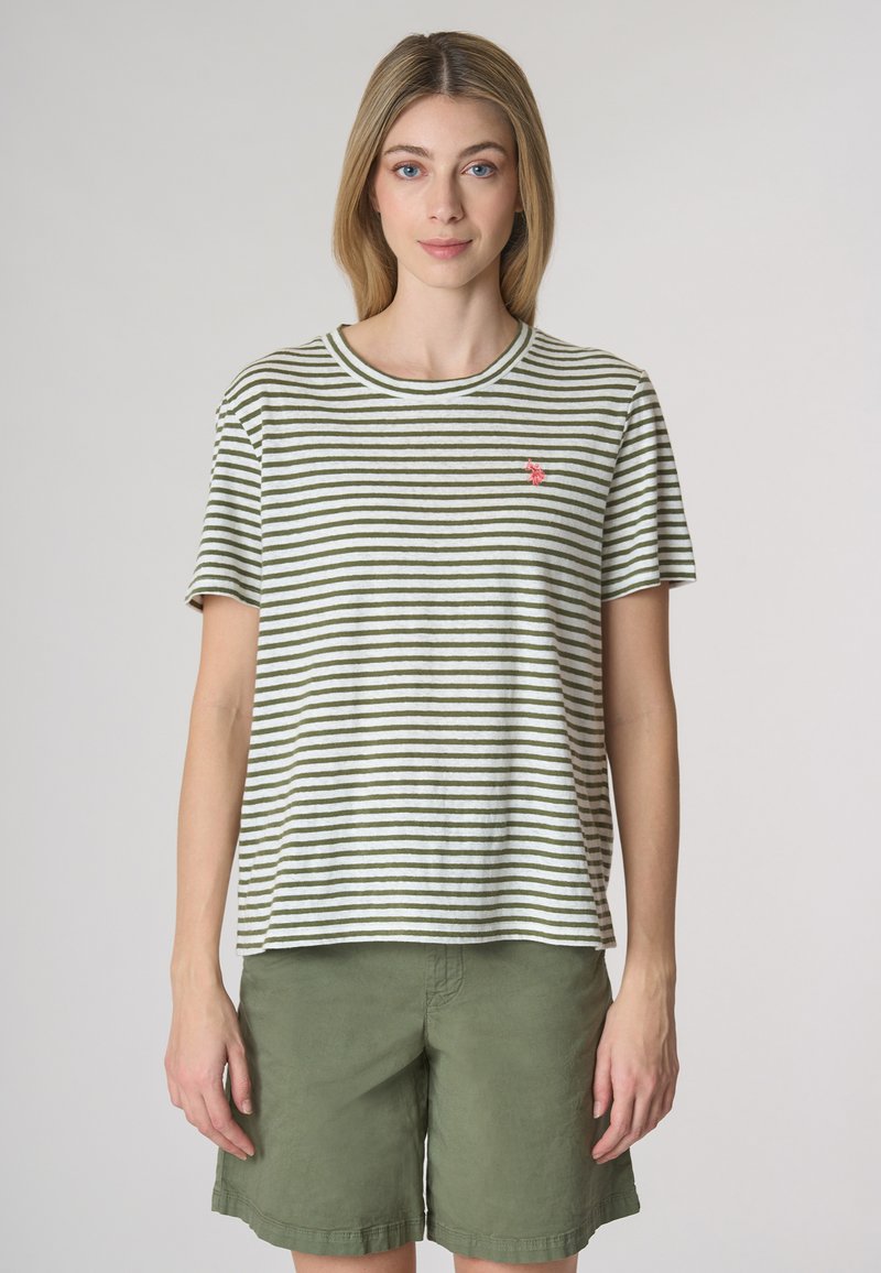 Camicia a maniche corte a righe in verde oliva e bianco, con scollatura rotonda e un piccolo logo rosa sul petto. Abbinata a pantaloni corti verdi.