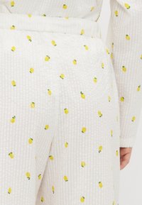 White textured fabric featuring a pattern of small yellow lemons and green leaves, with a comfortable, elastic waistband for ease of wear.