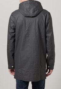 Veste imperméable gris foncé avec capuche, texture lisse, boutons-pression sur les poignets, et design à l'arrière plus long. Convient pour le temps pluvieux.
