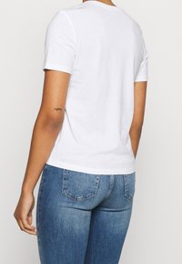 Hvid bomulds T-shirt med korte ærmer og rund halsudskæring, parret med blå denim jeans med en tætsiddende pasform og baglommer.