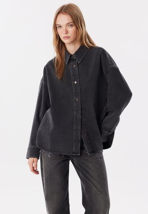 Schwarze Denim-Hemdjacke mit Knopfleiste, spitzem Kragen, oversized Passform und dezenten Distressed-Details. Weicher Stoff und strapazierfähiges Material.