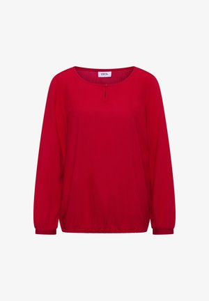 Blouse rouge à manches longues avec un col rond, taille froncée et un petit détail de bouton au centre devant. Texture de tissu lisse.