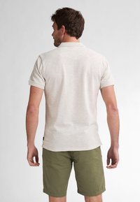 Ljus beige pikétröja med korta ärmar och krage, tillsammans med olivgröna shorts. Tyget har en subtil textur och en avslappnad passform.