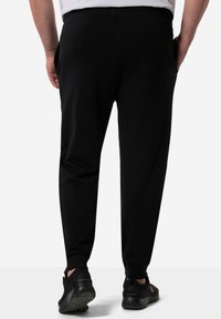 Zwarte joggers van zacht materiaal met een tapering ontwerp, een elastische tailleband en enkelsokken. Inclusief een achterzakdetail.