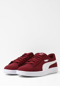 Zapatillas bajas sintéticas rojas con acentos blancos, que presentan cordones redondos, un collar acolchado y una suela de goma texturizada.