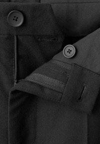 Crne hlače od tkanine s glatkom teksturom, s patentnim zatvaračem, dva gumba i detaljima šavova na pojasu i džepovima.