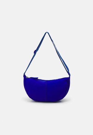 Blue crescent-shaped crossbody bag with adjustable strap and top zipper closure on a plain light background.