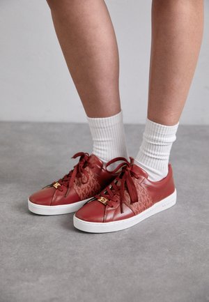 Sneakers basso in pelle rossa con pannello laterale texturizzato, punta tondeggiante, suola piatta bianca e dettagli decorativi in oro sui lacci.