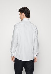 Weißes Hemd mit langen Ärmeln, Knopfmanschetten und einer glatten Textur. Verfügt über einen klassischen Kragen und subtile Details an den Manschetten.
