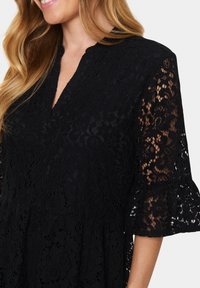 Black lace dress featuring a V-neckline, three-quarter sleeves with flared cuffs, and intricate floral patterns throughout.