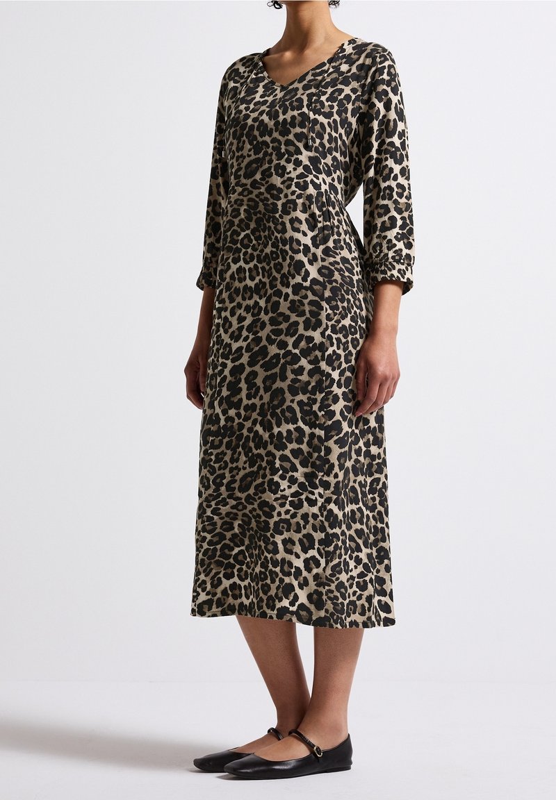 Femme portant une robe ample imprimé léopard longueur mollet avec manches trois-quarts et des ballerines Mary Jane noires sur un fond uni.