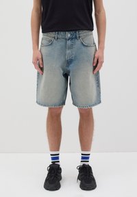 Shorts de mezclilla en un lavado claro, con corte recto, cinco bolsillos y cierre de botón. Llevados con zapatillas negras y calcetines de rayas.