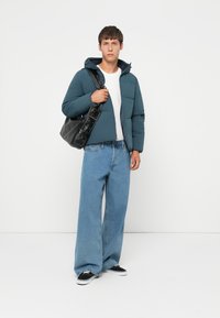 Teal puffer jacket with hood, white t-shirt underneath, wide-leg blue denim jeans, and black handbag, accompanied by black sneakers.