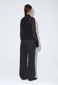 Musta, läpikuultava pitkähihaisen yläosa, jossa on vartalonmyötäinen leikkaus ja löysä selkäosa, yhdistetty korkeavyötäröisiin, leveälahkeisiin tummiin farkkuihin. Hienovaraiset ompeludetaljit.