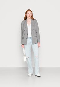 Blazer de dois botões em padrão pied-de-poule preto e branco, t-shirt branca com decote em V, jeans desgastados azul claro e sapatilhas brancas.