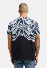 Svart t-skjorte med korte ermer som har et teksturert hvitt bølgemønster på den øverste halvdelen. Stoffet ser glatt ut med vanlig passform.