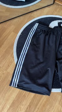 Calções atléticos pretos feitos de um tecido suave, apresentando três riscas verticais brancas ao longo do lado e um bolso com fecho.}}
