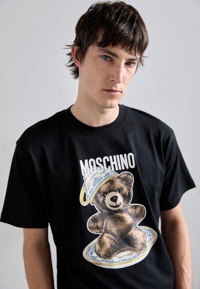 T-shirt en coton noir avec un graphique d'ours présentant un plat bleu et jaune, marqué "Moschino" en lettres blanches en gras au-dessus du design.