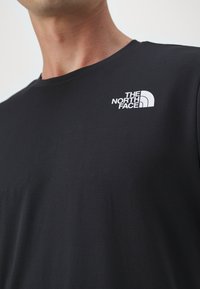 T-shirt preto de mangas curtas feito de um tecido suave com decote redondo. Apresenta um logo branco da "The North Face" no lado superior esquerdo do peito.