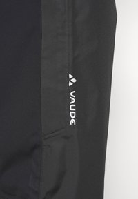 Pantalons de sport noirs au design épuré, fabriqués en tissu léger, avec un logo "Vaude" blanc contrastant sur le côté.