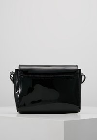 Borsa in pelle patent nera con forma rettangolare, pattina ripiegabile e piccole maniglie laterali. Texture liscia e lucida, design minimalista.