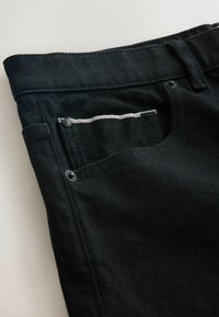Black denim jeans with a front pocket, silver stitching along the pocket edge, and distinct metal hardware accents.