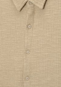 Beiges Hemd mit Kragen aus strukturiertem Stoff mit Karomuster. Verfügt über vier Knöpfe auf der Vorderseite und eine weiche Oberfläche.