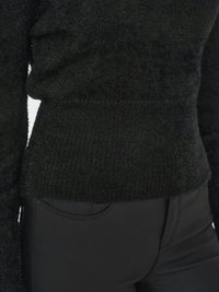 Pull en maille noire avec une finition texturée, doté d'une taille ajustée et de longues manches, associé à un pantalon noir élégant.
