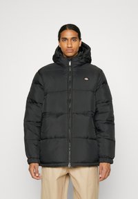 Schwarze Steppjacke mit Reißverschluss und Kapuze. Verfügt über eine gesteppte Polsterung und elastische Bündchen zur Isolierung. Kleines Logo auf der Brust.