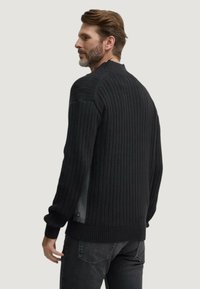 Maglione a costine nere con colletto alto e maniche lunghe, caratterizzato da un sottile accento del logo. Il tessuto è texturizzato e aderente.