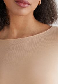 Haut en tissu élastique nude avec un col large et lisse et une texture douce, affichant un éclat subtil et des finitions propres aux bords.